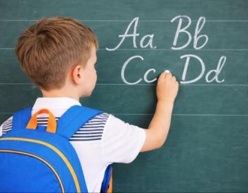 Schulkind Ein Junge schreibt mit Kreide an eine Schultafel