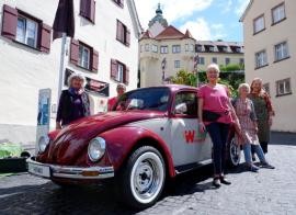 Die Gärtnerinnen und der mit Kräutern bepflanzte, rot-weiße VW Käfer, im Hintergrund die Basilika