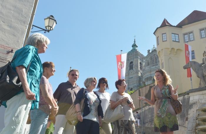 Gäste lauschen einer Stadtführerin, im Hintergrund die Basilika