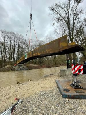 Ein Kran transportiert eine Brückenkonstruktion über den Fluss