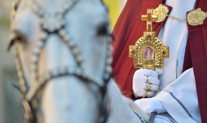 Ein Pferd, dahinter eine Hand mit weißem Handschuhe, die eine goldene Reliquie hält