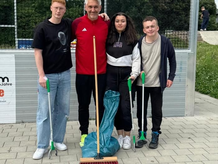 Vier Personen mit Besen, Greifzangen und Müllsäcken