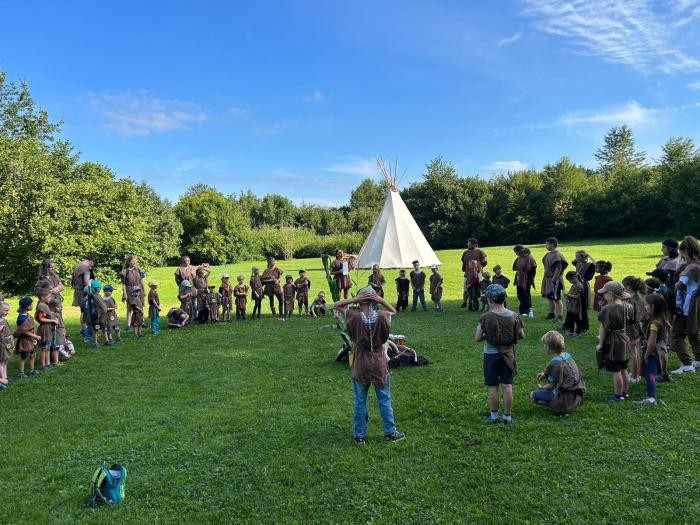 Ein weißes Tipi steht auf einer Wiese, vorne ca. 30 Kinder