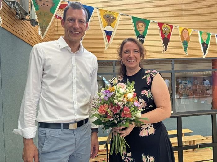 Eine Frau mit Blumenstrauß lächelt, neben ihr ein Mann, der ihr gratuliert