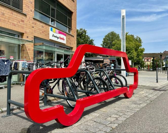 Der lebensgroße rote Umriss eines Autos steht auf einem Parkplatz. An dem Modell sind viele Fahrräder geparkt