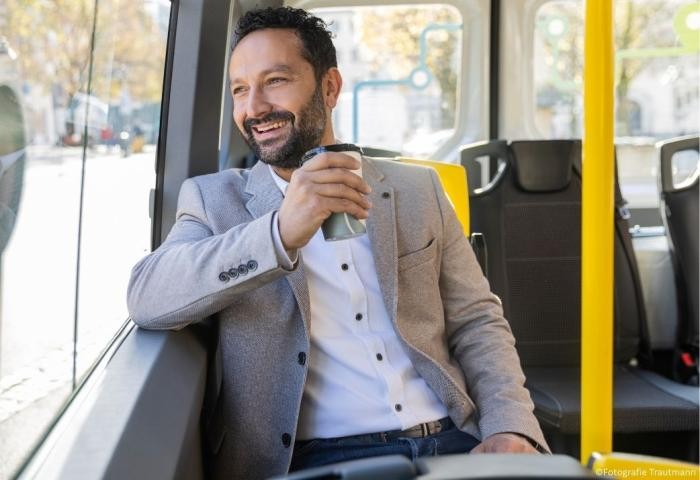 Mit dem ÖPNV zuverlässig, bequem und umweltbewusst durch die Stadt Junger Mann sitzt im Bus und schaut lachend aus dem Fenster.