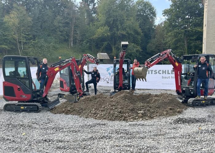 Vier Männer stehen an vier roten Minibaggern an einer Baugrube.