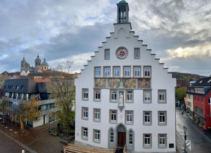 Die Gebäudefassade strahlt Weiß, im Hintergrund Wolken am Himmel
