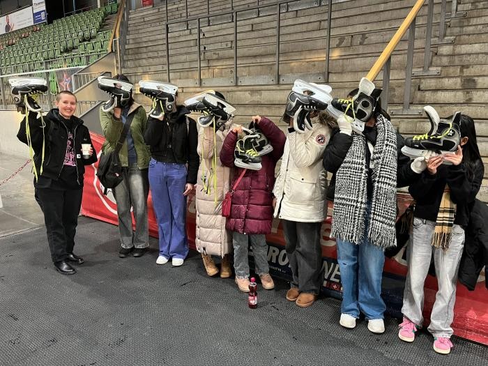 Gruppenbild mit acht Personen, die Schlittschuhe in der Hand halten
