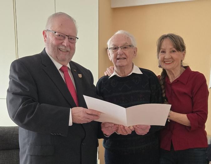Zwei Männer und eine Frau lächeln in die Kamera. Sie halten eine Urkunde in der Hand.