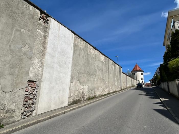 Eine lange weiße Mauer mit Rissen und Flecken entlang einer Straße