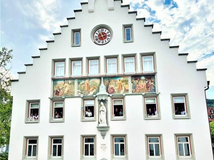 Ein Gebäude, aus dessen geöffneten Fenstern viele Menschen winken