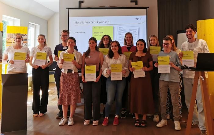 Viele junge Menschen bei einem Gruppenfoto in einem Raum. Sie halten ein Dokument in der Hand