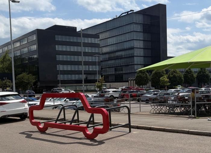 Ein Gebäude im Hintergrund. Im Vordergrund der Umriss eines Autos aus Metall in rot