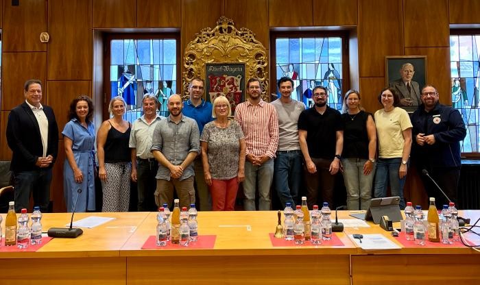 Das Gruppenbild zeigt Männer und Frauen allen Alters, die in einem holzgetäfelten Saal stehen