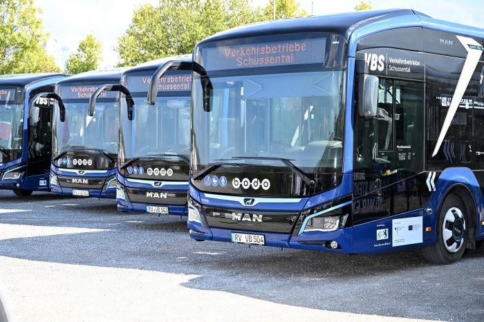 Vier blaue Omnibusse stehen nebeneinander auf einem Parkplatz