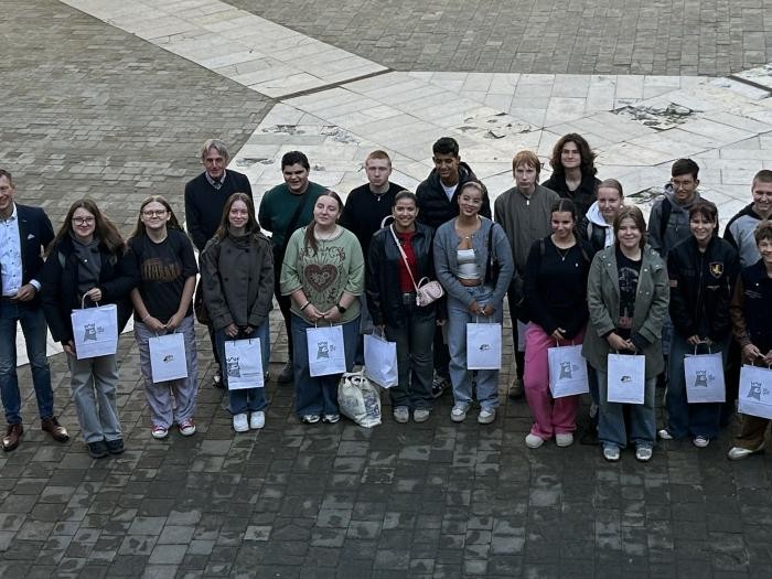 Ein Gruppenbild mit vielen jungen Menschen, die Papiertaschen in der Hand halten und lächelnd in die Kamera blicken