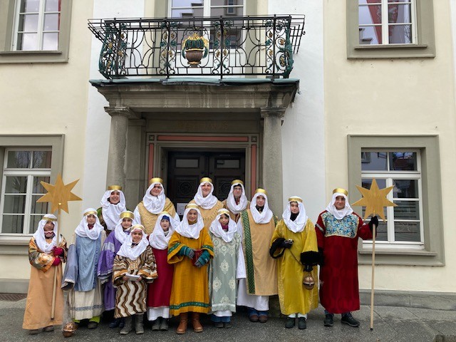 Gruppenbild mit vielen Kindern, die mit Gewändern als Könige verkleidet sind. Zwei halten große Sterner aus Holz in der Hand.